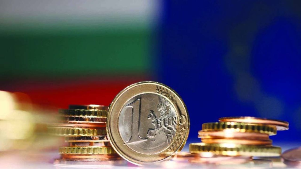 A one Euro coin and coin stacks in front of blurred Bulgarian and European Union flags
