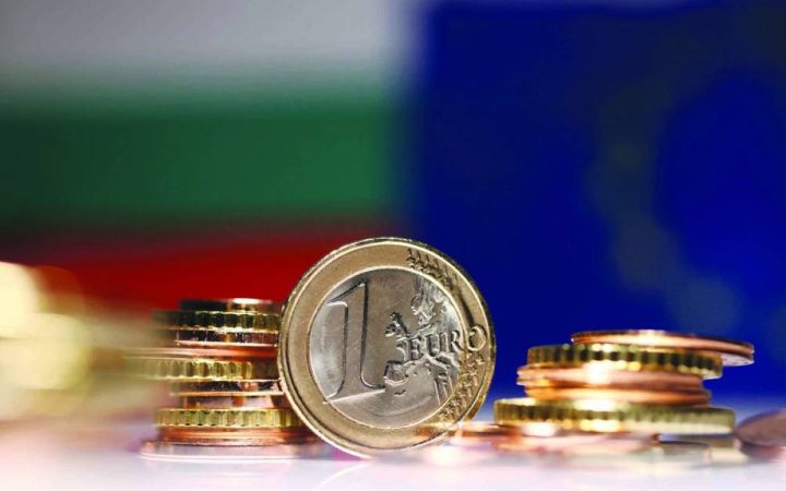 A one Euro coin and coin stacks in front of blurred Bulgarian and European Union flags