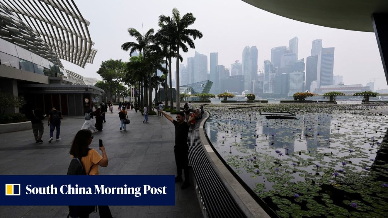 Tourists on the promenade overlooking the Marina Bay skyline in Singapore on an overcast day