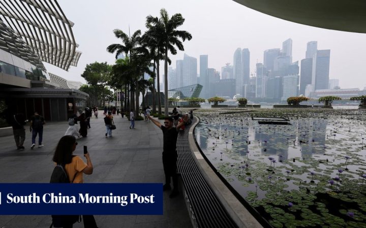Tourists on the promenade overlooking the Marina Bay skyline in Singapore on an overcast day