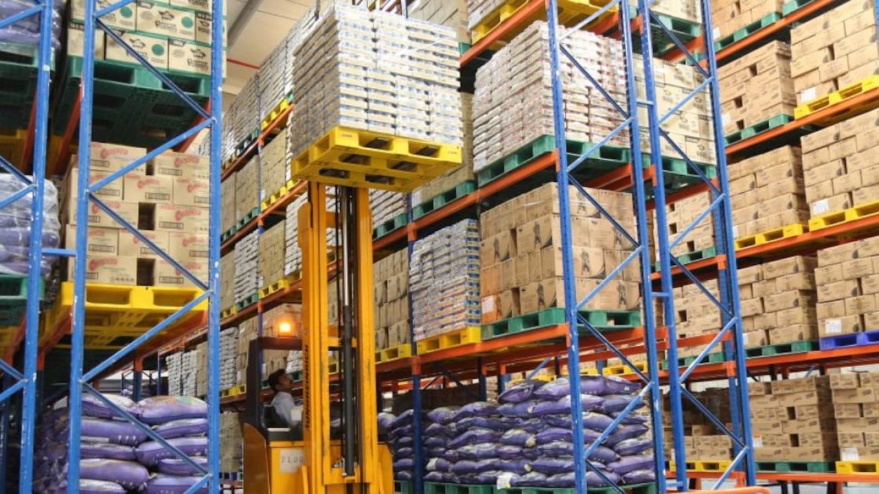 Forklift lifting a loaded pallet inside a large industrial warehouse with high-bay shelving