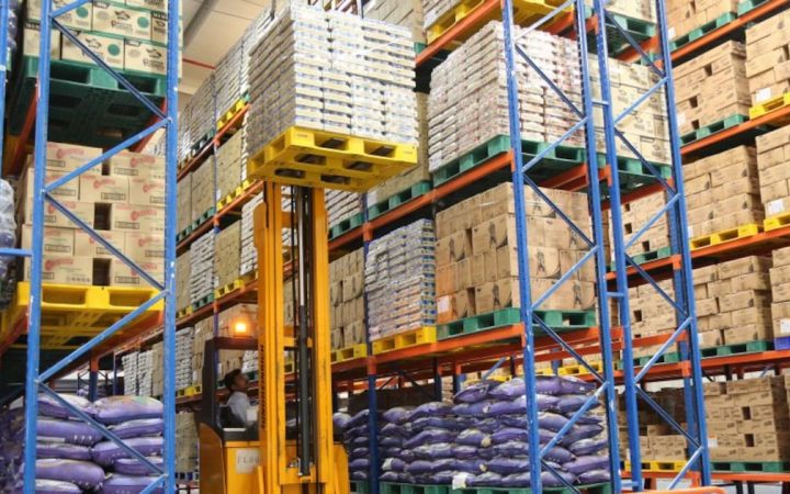 Forklift lifting a loaded pallet inside a large industrial warehouse with high-bay shelving