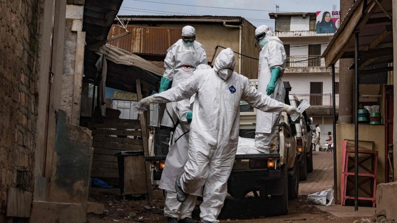 Health workers wearing full protective hazmat suits and masks stepping off a pickup truck in a street