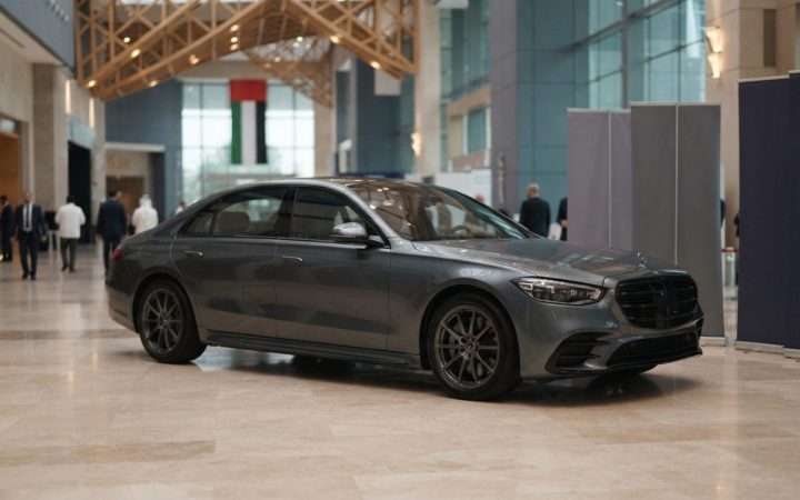 Illustration: A modern luxury executive sedan displayed inside an opulent marble-floored exhibition hall in Abu Dhabi, softly illuminated by architect