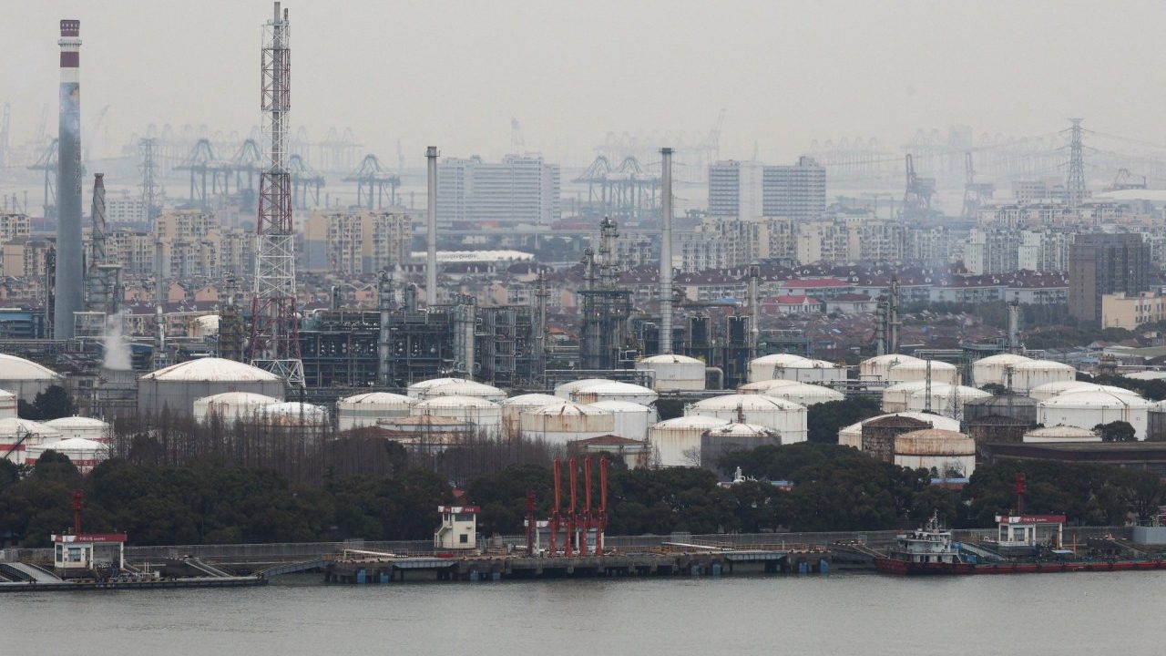 Industrial petrochemical refinery and storage tanks along a waterfront under a hazy sky