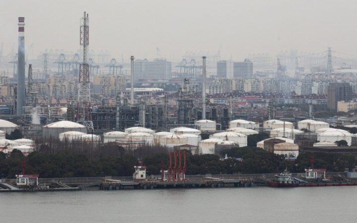 Industrial petrochemical refinery and storage tanks along a waterfront under a hazy sky