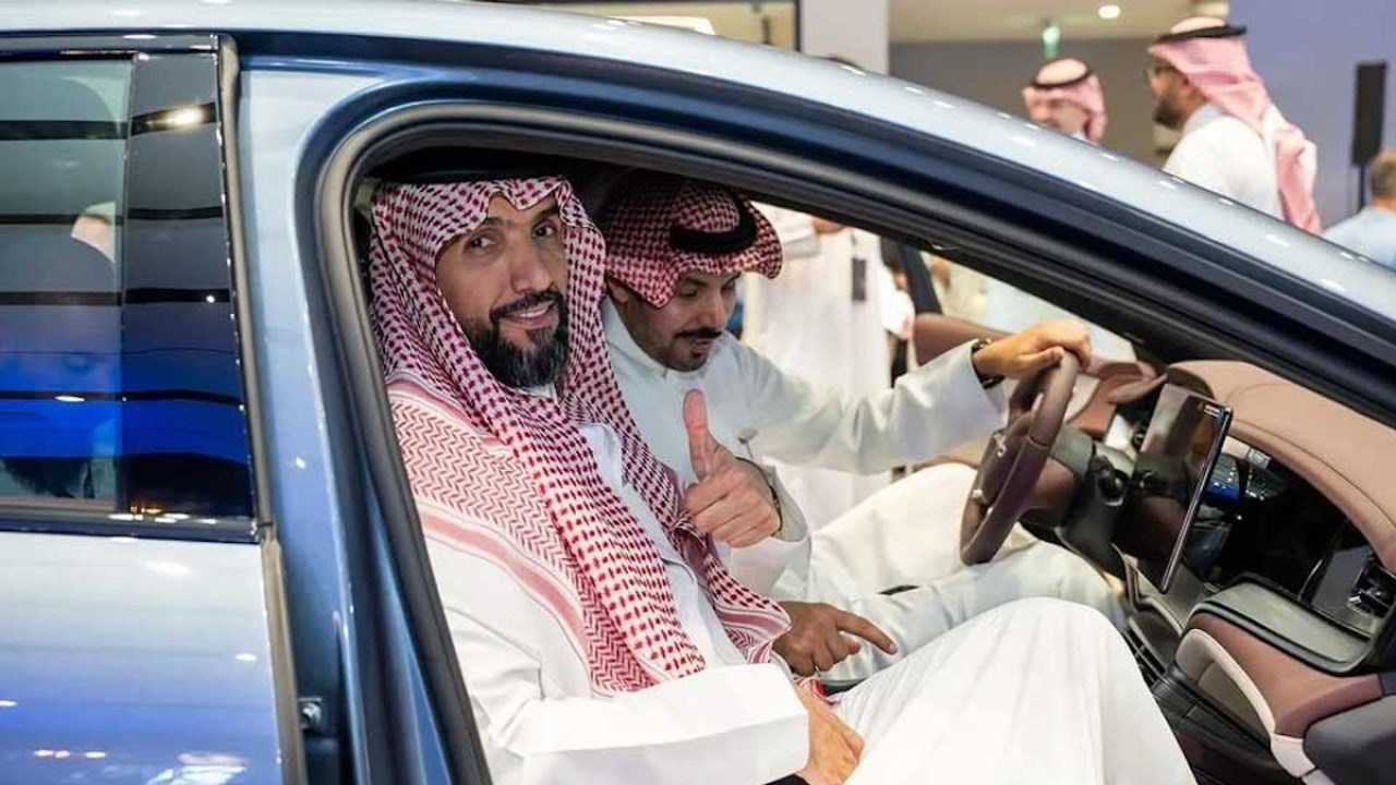 Men in traditional Gulf attire exploring the interior of an electric vehicle at an automotive exhibition
