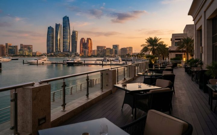 Illustration: An elegant luxury hotel waterfront terrace in Abu Dhabi at sunset, overlooking calm marina waters with modern architectural skyline in t