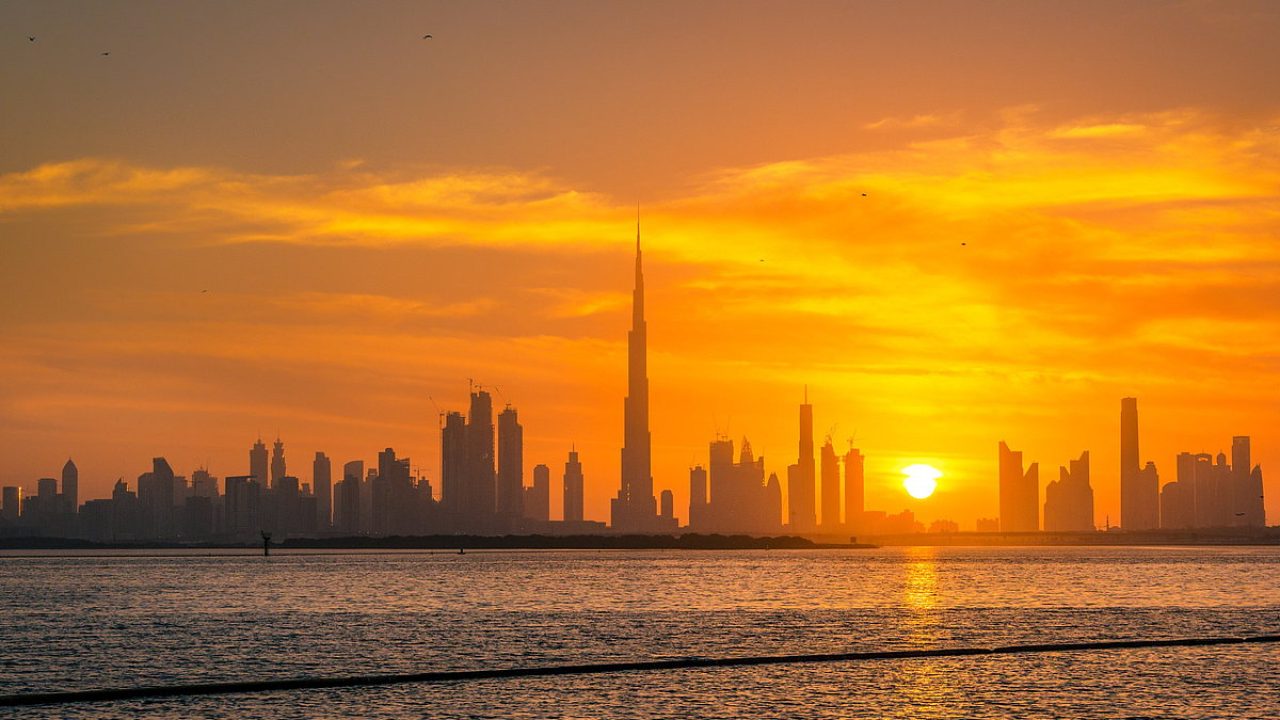 Dubai skyline with Burj Khalifa silhouetted against a golden sunset over the water
