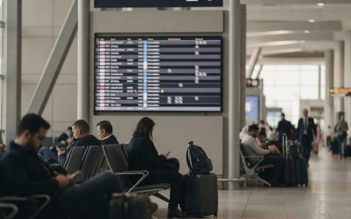 Illustration: An airport flight information display board showing multiple delayed and cancelled flight listings in an international terminal, with tr