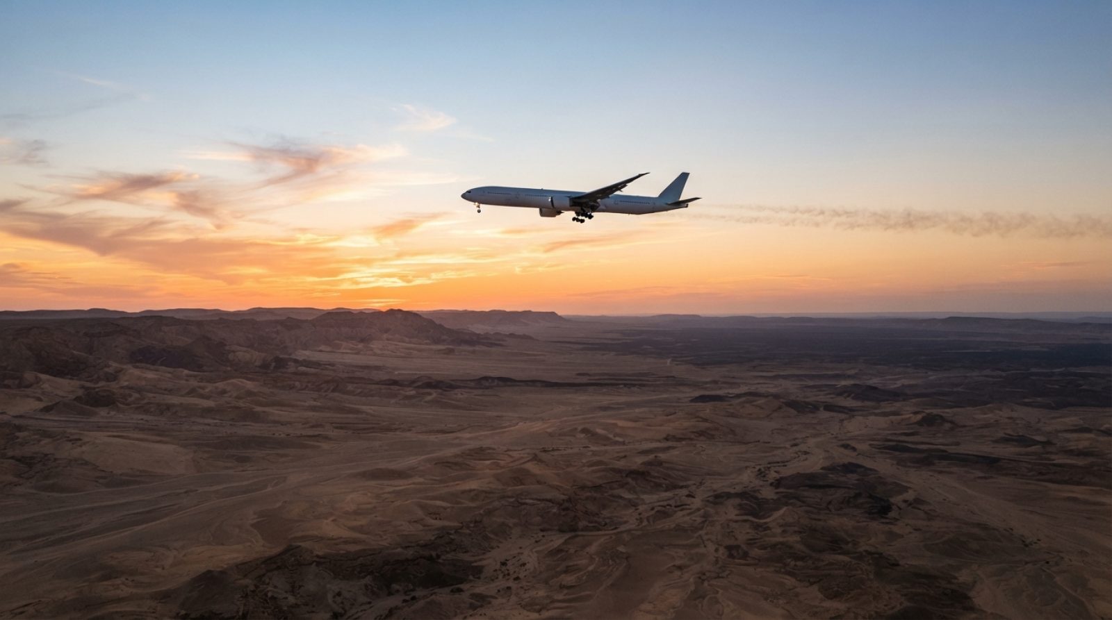 Illustration: A commercial wide-body airplane flying at high altitude above an expansive arid desert landscape at sunset, seen from below against an e