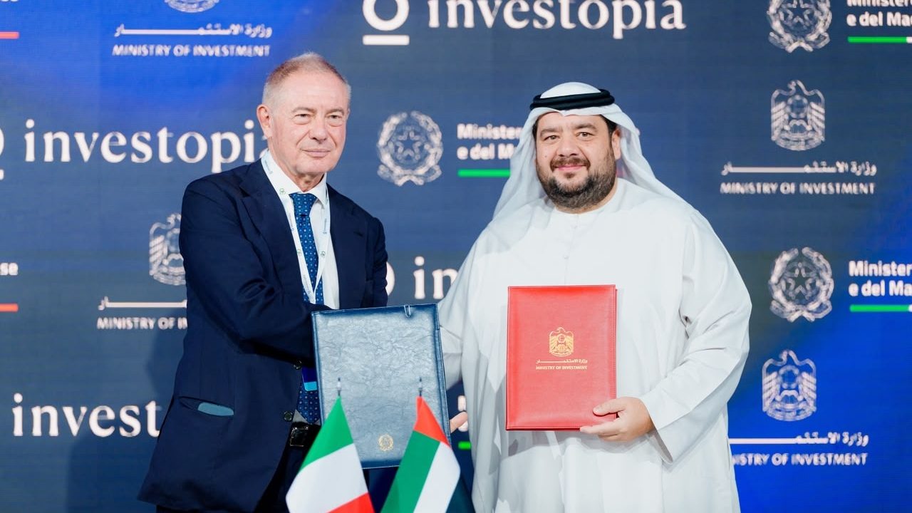 Two officials exchange signed bilateral agreements before UAE and Italian flags at an Investopia conference