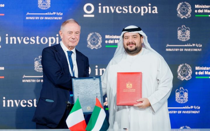 Two officials exchange signed bilateral agreements before UAE and Italian flags at an Investopia conference