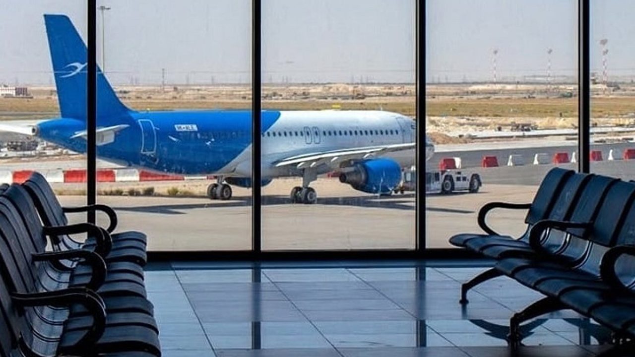 Airplane parked on an airport tarmac seen through terminal windows with empty seats in the foreground