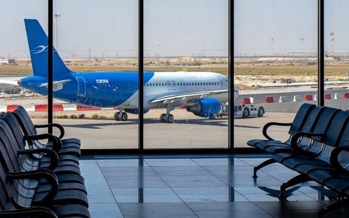 Airplane parked on an airport tarmac seen through terminal windows with empty seats in the foreground