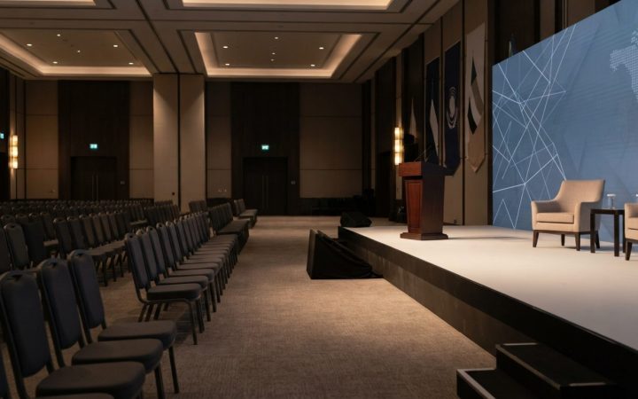 Illustration: An empty modern corporate conference hall and stage in Dubai set up for an international bilateral business forum, featuring ambient war