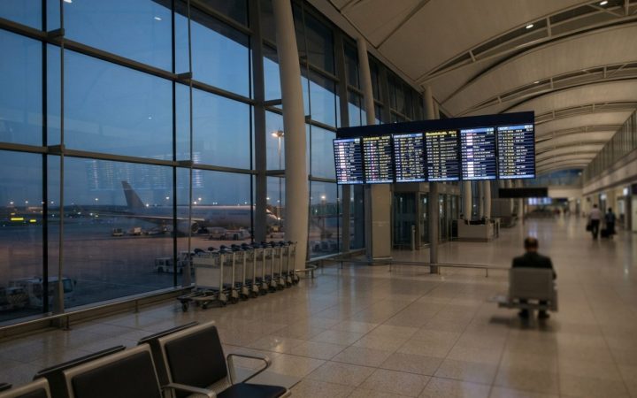 Illustration: An empty international airport departure hall with electronic flight status boards showing regional routes, luggage trolleys standing id