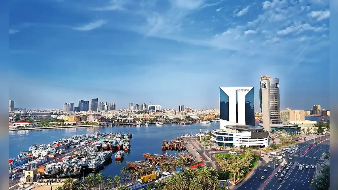 Panoramic view of Dubai Creek, traditional dhow boats, and the Dubai Chamber building under a blue sky