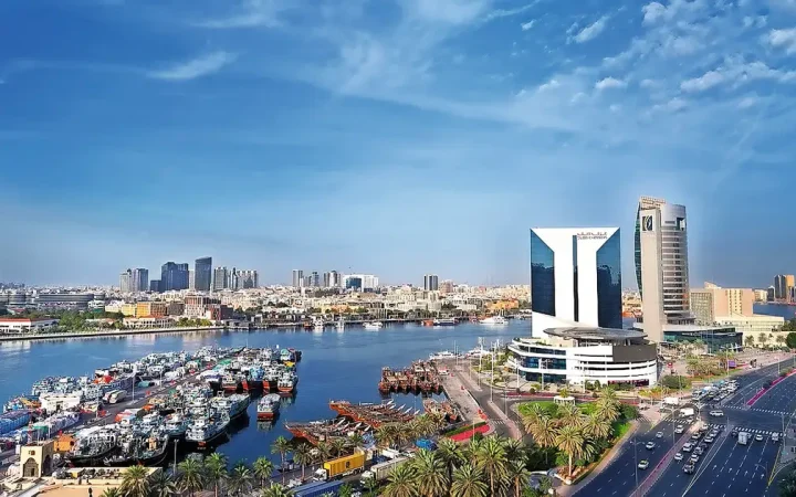 Panoramic view of Dubai Creek, traditional dhow boats, and the Dubai Chamber building under a blue sky
