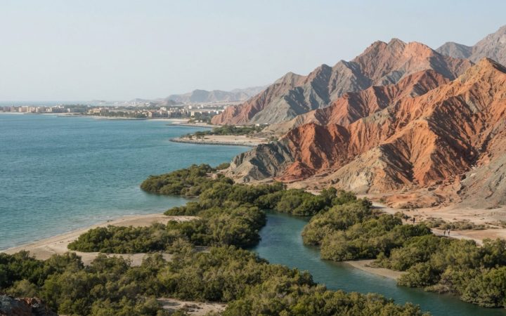 Illustration: Editorial photograph showing the coastal and mountain scenery of Ras Al Khaimah, featuring rugged red mountain ridges meeting calm Arabi