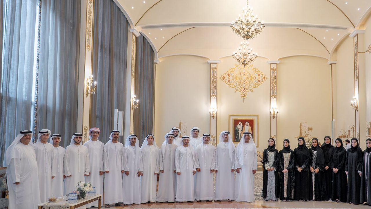 Group of Emirati men and women in traditional attire standing in an ornate reception hall