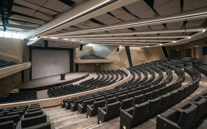 Illustration: A wide interior view of a modern, empty international convention center and auditorium in Riyadh, showing tiered amphitheater seating, c