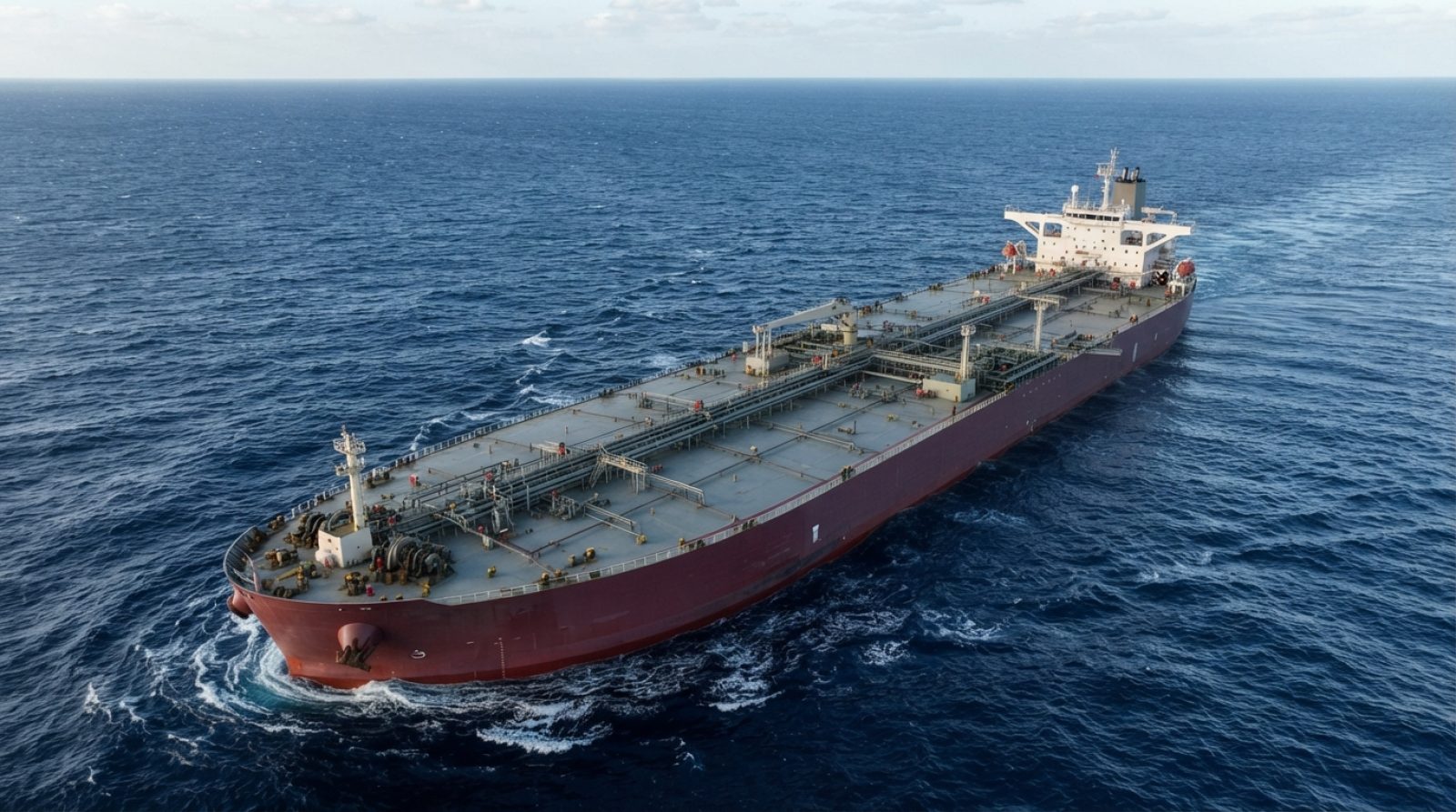 Illustration: A very large crude carrier tanker vessel navigating open deep blue seas under daylight, high-angle aerial photograph showing deck cargo