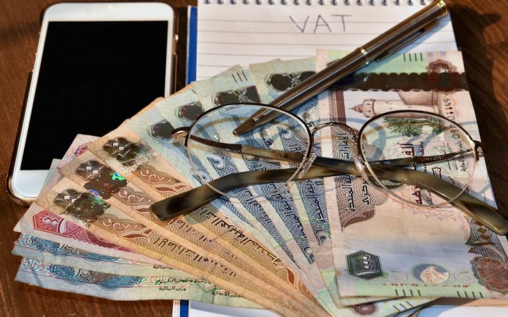 UAE dirham banknotes arranged with eyeglasses, a pen, a smartphone, and a notepad reading VAT