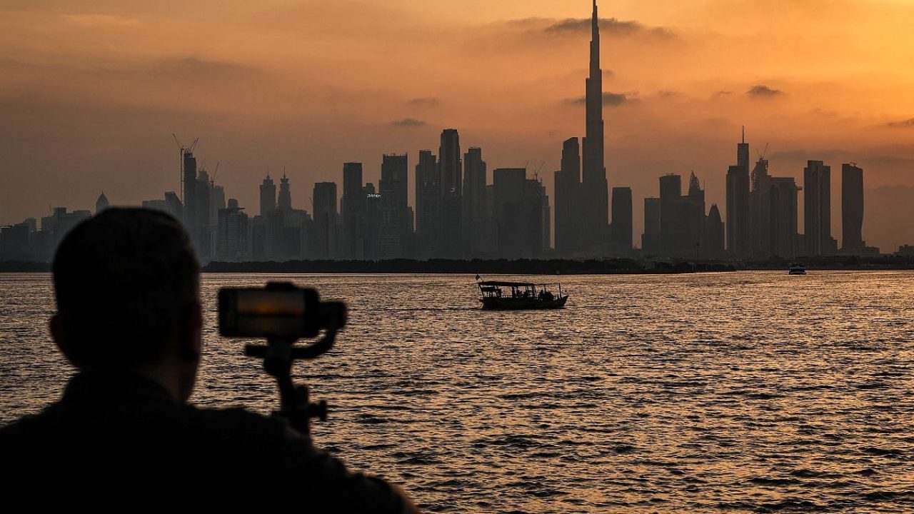 Silhouette of a person filming the Dubai skyline with Burj Khalifa across the water at sunset