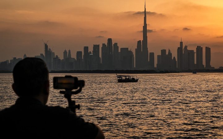 Silhouette of a person filming the Dubai skyline with Burj Khalifa across the water at sunset
