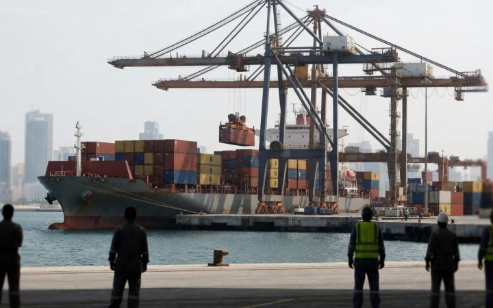 Illustration: Commercial cargo vessel docked at an industrial port with shipping containers being handled by cranes under daylight, representing inter