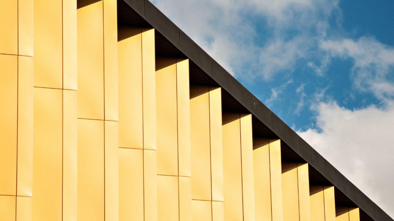 Modern yellow architectural facade detail against a blue sky with white clouds
