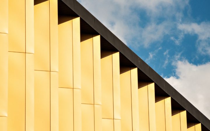 Modern yellow architectural facade detail against a blue sky with white clouds