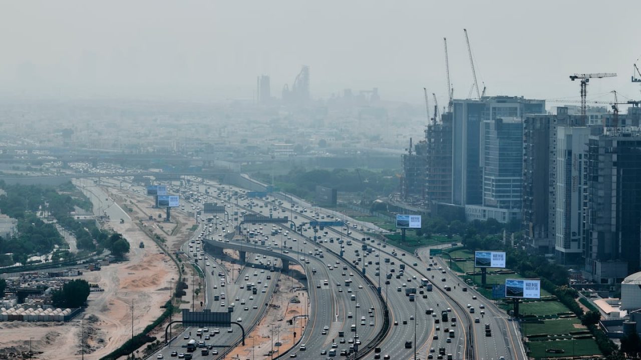 Aerial view of a busy multi-lane highway lined with construction and skyscrapers under heavy haze