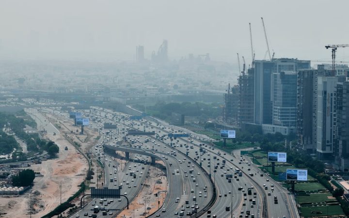 Aerial view of a busy multi-lane highway lined with construction and skyscrapers under heavy haze