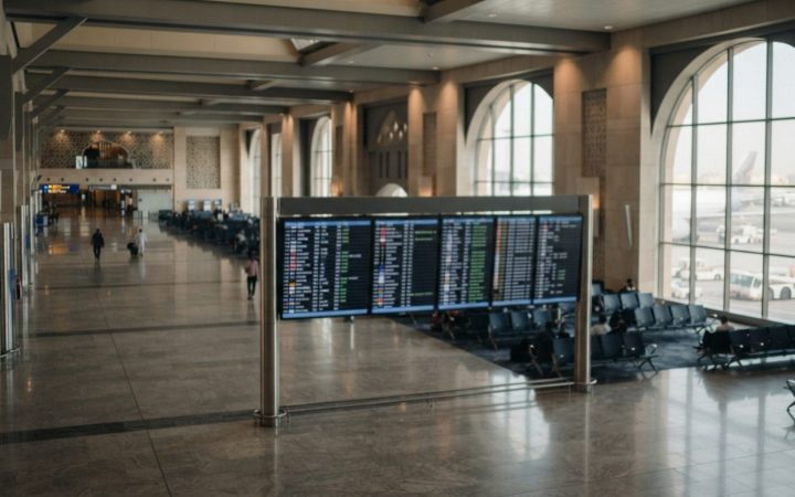 Illustration: An international airport departure terminal showing electronic flight information boards with schedule updates, with an empty concourse