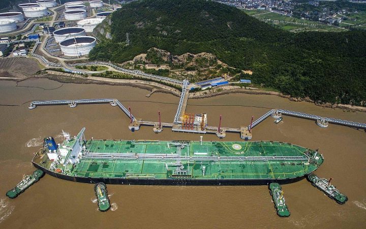 Aerial view of a large crude oil tanker docking at an offshore terminal jetty with tugboats