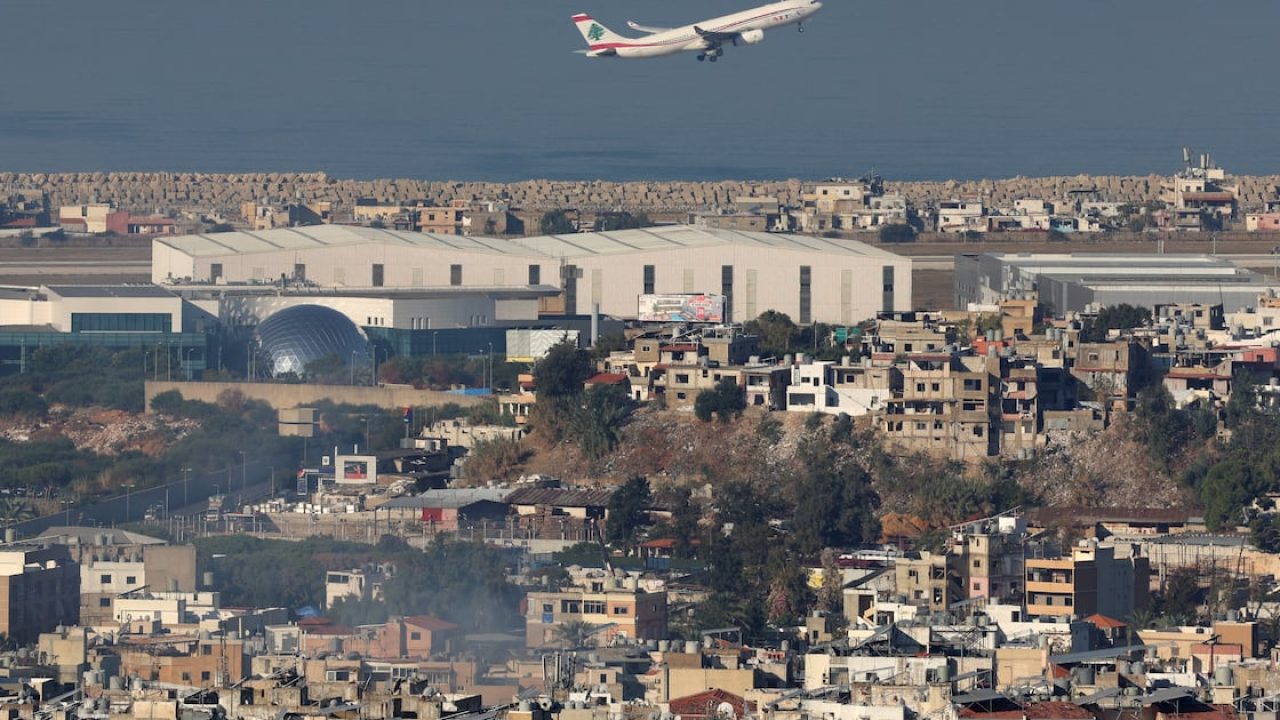 Airplane flying over a dense urban landscape near an airport runway by the sea