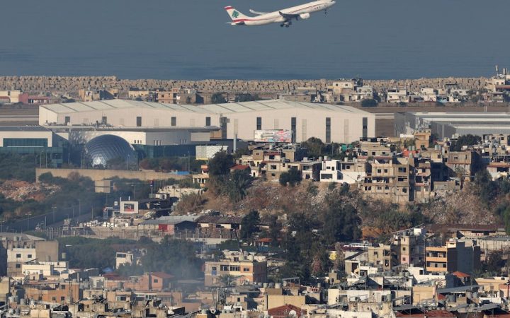 Airplane flying over a dense urban landscape near an airport runway by the sea